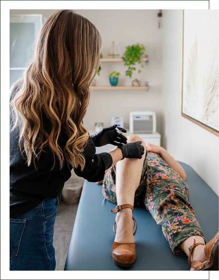 A person wearing gloves examines or treats another person’s knee as they lie on an exam table in a medical or wellness office.